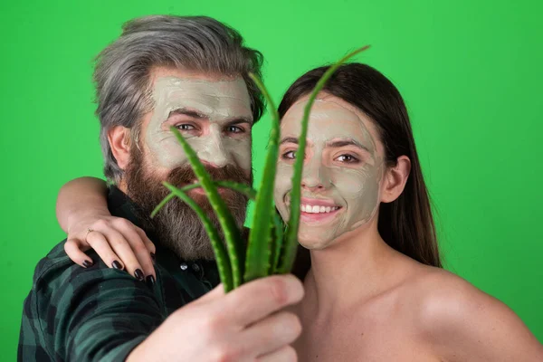 楽しいカップルのための顔の緑のマスク。面白いカップルはアロエベラと顔のケアを取得します.美容師は男と女の顔に顔マスクを作っている。美容師作るフェイシャルプロシージャとともにアロエベラ. — ストック写真