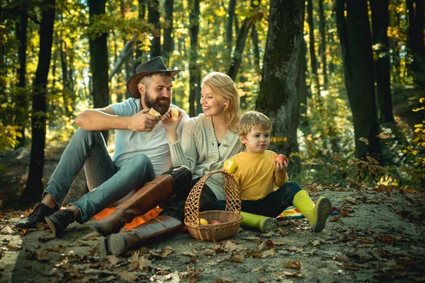 Lycklig familj på tre som ligger i gräset på hösten. En ung familj med ett litet barn som har picknick i höstnaturen vid solnedgången. En sols ljus. Lycklig familj i parken kvällsljus. — Stockfoto