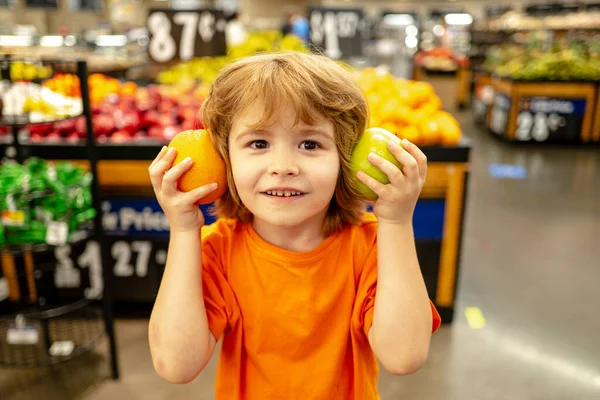 Piccolo ragazzo carino con carrello pieno di verdure fresche biologiche e frutta in piedi nel reparto di alimentari o supermercato. Bambino carino con carrello della spesa con prodotti . — Foto Stock