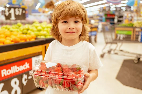 Piccolo ragazzo felice con fragola, shopping al supermercato, negozio di alimentari. Un ragazzo sta facendo shopping in un supermercato. Supermercato, Shopping con Bambino . — Foto Stock