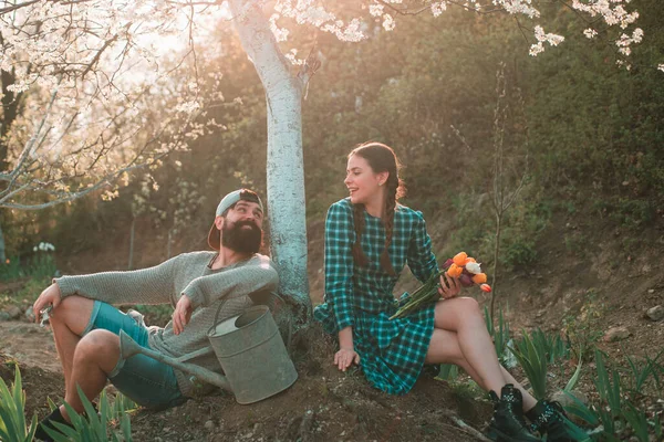 Amici seduti sull'erba nel giardino primaverile. Gioventù in cortile primavera con attrezzi da giardino. Rilassante dopo un duro lavoro . — Foto Stock