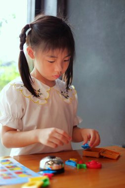 Tahta bir masadaki masa oyunundan çıkan renkli plastik oyuncaklarla oynayan sevimli bir Asyalı kız..