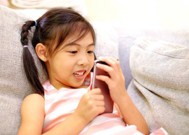 Kanepede akıllı telefonuyla oynayan genç bir Asyalı kız.