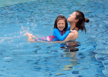 Bir anne kızına yüzmeyi öğretiyor, gülümsüyor ve birlikte eğleniyor..