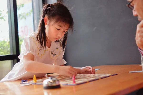 Çekici bir Asyalı anaokulu kızı büyükbabasıyla masa oyunu oynamayı öğreniyor.