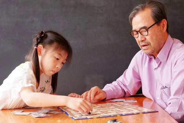 Büyükbabasıyla masa oyunu oynamayı öğrenen Asyalı tatlı bir anaokulu kızı.