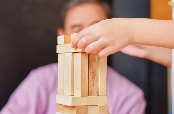 An grandfather is teaching his granddaughter to play a block wood tower game.