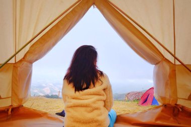 Sabahları beyaz çadırında huzur içinde oturan genç bir kadın serin bir esinti ve sabah güneşiyle esniyor ve dinleniyor..