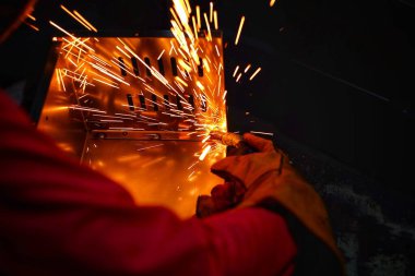 Pembe uzun kollu ceket giyen Hintli bir kadın, güvenlik maskesi ve deri eldivenler, bilgisayar sunucusu rafı için metal bir çanta kaynak yapıyor, kıvılcımlar.