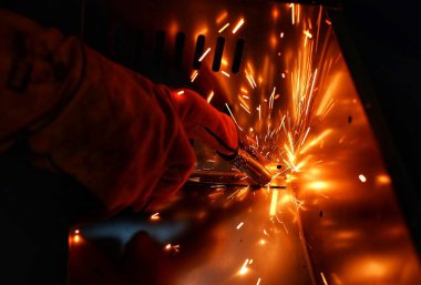 Pembe uzun kollu ceket giyen Hintli bir kadın, güvenlik maskesi ve deri eldivenler, bilgisayar sunucusu rafı için metal bir çanta kaynak yapıyor, kıvılcımlar.