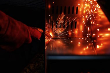 Pembe uzun kollu ceket giyen Hintli bir kadın, güvenlik maskesi ve deri eldivenler, bilgisayar sunucusu rafı için metal bir çanta kaynak yapıyor, kıvılcımlar.