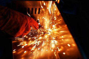 Pembe uzun kollu ceket giyen Hintli bir kadın, güvenlik maskesi ve deri eldivenler, bilgisayar sunucusu rafı için metal bir çanta kaynak yapıyor, kıvılcımlar.