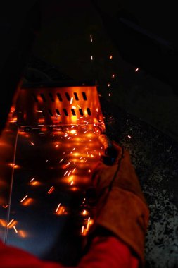 Pembe uzun kollu ceket giyen Hintli bir kadın, güvenlik maskesi ve deri eldivenler, bilgisayar sunucusu rafı için metal bir çanta kaynak yapıyor, kıvılcımlar.