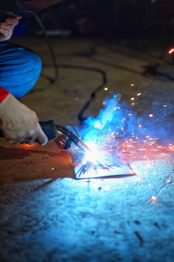 Pembe ceketli ve koruyucu eldivenli Hintli bir kadın bir kaynakçıyı kıvılcım ve dumanla test ediyor.