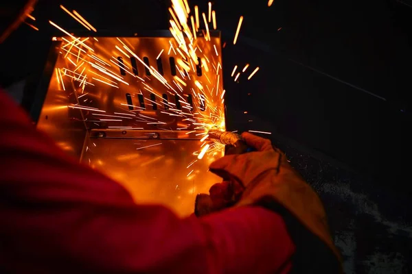 Pembe uzun kollu ceket giyen Hintli bir kadın, güvenlik maskesi ve deri eldivenler, bilgisayar sunucusu rafı için metal bir çanta kaynak yapıyor, kıvılcımlar.