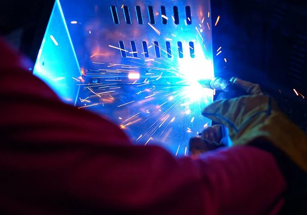 Pembe uzun kollu ceket giyen Hintli bir kadın, güvenlik maskesi ve deri eldivenler, bilgisayar sunucusu rafı için metal bir çanta kaynak yapıyor, kıvılcımlar.