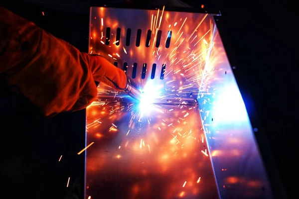 Pembe uzun kollu ceket giyen Hintli bir kadın, güvenlik maskesi ve deri eldivenler, bilgisayar sunucusu rafı için metal bir çanta kaynak yapıyor, kıvılcımlar.