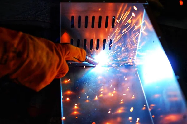 Pembe uzun kollu ceket giyen Hintli bir kadın, güvenlik maskesi ve deri eldivenler, bilgisayar sunucusu rafı için metal bir çanta kaynak yapıyor, kıvılcımlar.