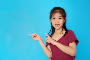 Çekici bir Asyalı ergen kızın belden yükseklik çekimi. Bir ürün sunuyor, açık mavi düz bir arkaplanı işaret ediyor..