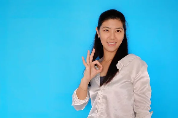一位年轻貌美的亚洲女人用右手做了一个很好的手势 确认一切都很好 浅蓝色背景 — 图库照片