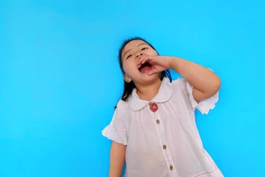 Sevimli genç Asyalı bir kız heyecan verici hissediyor. Ağzını sonuna kadar açıp avucunu ağzında tutarak avazı çıktığı kadar bağırıyor. Düz açık mavi arkaplan.