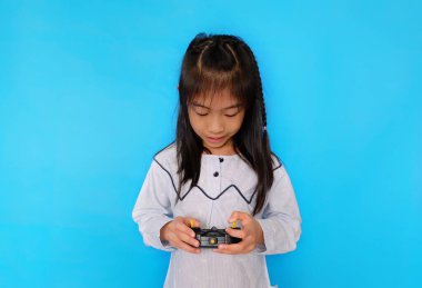 Şirin bir Asyalı kız uzaktan kumandalı radyo vericisiyle oynuyor. Düz açık mavi arkaplan.