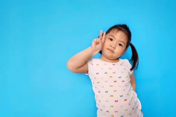 Genç ve tatlı bir Asyalı kız iki parmağıyla zafer işareti yapıyor. Düz açık mavi arkaplan.