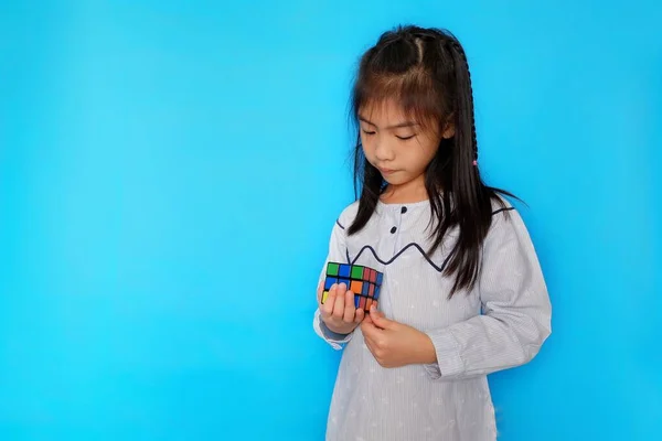 Genç ve tatlı bir Asyalı kız bir Rubik küpüyle oynuyor, öğrenirken eğleniyor. Düz açık mavi arkaplan.