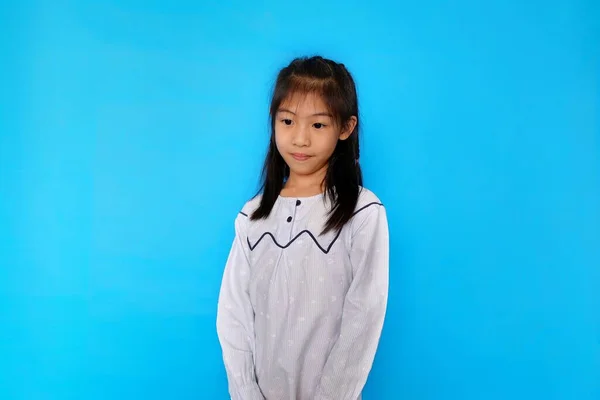 Çekici bir Asyalı reşit olmayan kızın portresi açık mavi bir arka planda duruyor, gülümsüyor..