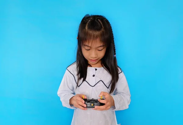 Şirin bir Asyalı kız uzaktan kumandalı radyo vericisiyle oynuyor. Düz açık mavi arkaplan.