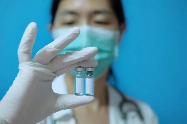 Bir klinikte ameliyat maskesi ve beyaz lastik eldivenli kadın bir asyalı doktor elinde boş beyaz etiketli iki cam aşı şişesi tutuyor..