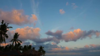Bir renkli zaman atlamalı video kümülüs bulutlar günbatımı sırasında hareketli ve değişen şekli. Palmiye ağaçları ve geleneksel nipa çatı ön planda görülebilir.
