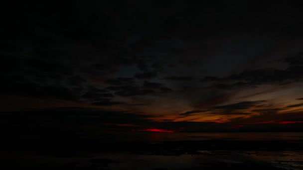 Une vidéo complète et cramoisie du lever du soleil sur les rives de Dumaguete City (à partir de l'obscurité). On peut voir les habitants ramasser des coquillages dans les bassins peu profonds laissés par la marée basse. Des silhouettes de bateaux de pêche peuvent également être vues au loin .