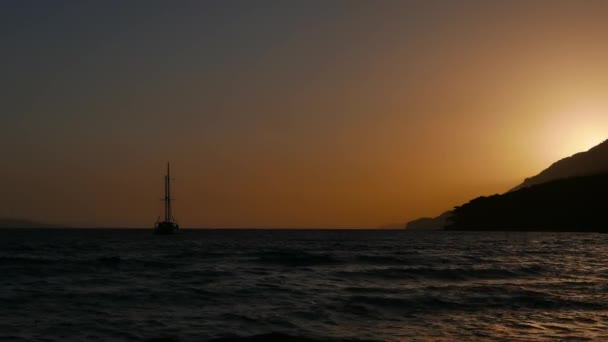 Vidéo d'un coucher de soleil sombre avec un ciel dégagé depuis la plage d'Akyaka (golfe de Gokova, mer Égée). Le soleil se couche derrière la cape. La silhouette d'un yacht peut également être vue .