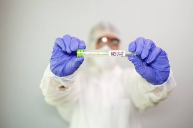 Üzerinde Coronavirus aşısı olan bir şırınga bulunan mavi cerrahi eldivenli mikrobiyolog ya da tıp çalışanı elinin yakın çekimi. COVID-19 aşı konsepti