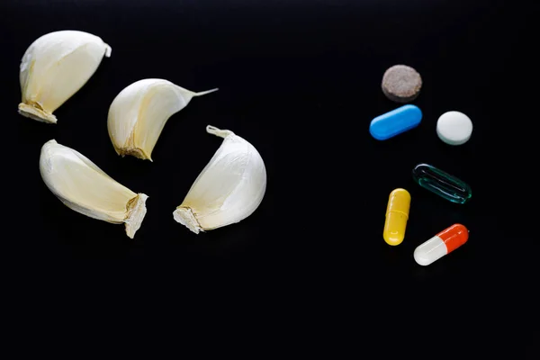 Sarımsak karanfilleri ve ilaç hapları siyah arka planda izole edilmiş ve fotokopi alanı var. Geleneksel doğal homeopat tıbbına karşı kimyasal haplar yapay tıp konsepti