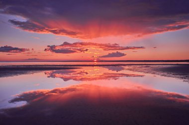 Dramatic reflection of the sky and sun rays in the water during a red sunset. clipart