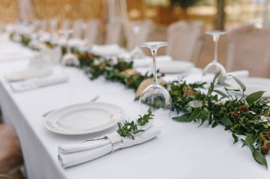 Deniz usulü şenlikli bir akşam yemeği servis ediyor, masada beyaz bir masa örtüsü, beyaz tabaklar, cam şarap bardakları.