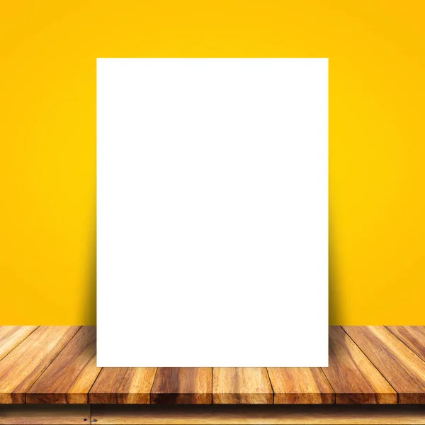 Cartel de papel blanco apoyado en la pared amarilla y la mesa de madera . —  Fotos de Stock