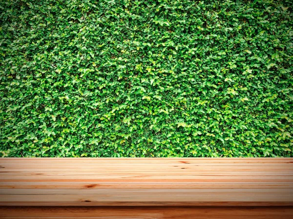 녹색 나뭇잎 벽에 나무 테이블. — 스톡 사진