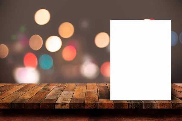 Cartel de papel blanco apoyado en mesa de madera con luz abstracta bokeh — Foto de Stock