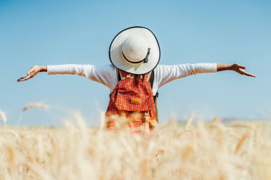 Altın buğday tarlasında duran genç kadın.