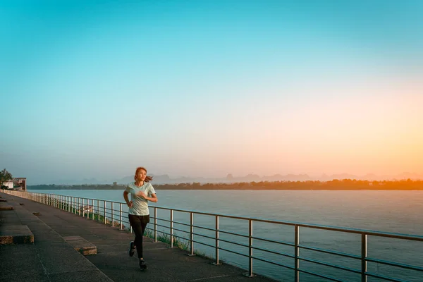 Woman running on street with a view of river in the morning.