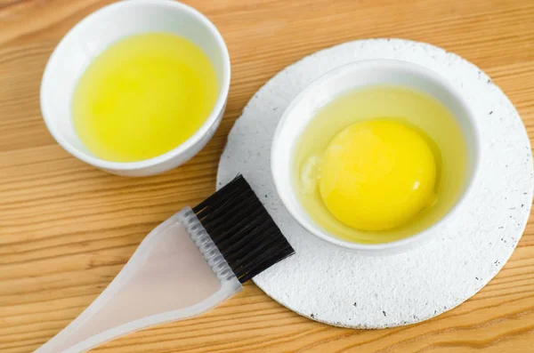 Telur mentah dan minyak zaitun dalam mangkuk keramik kecil untuk mempersiapkan wajah buatan sendiri dan masker rambut. Bahan untuk kosmetik diy . Stok Foto