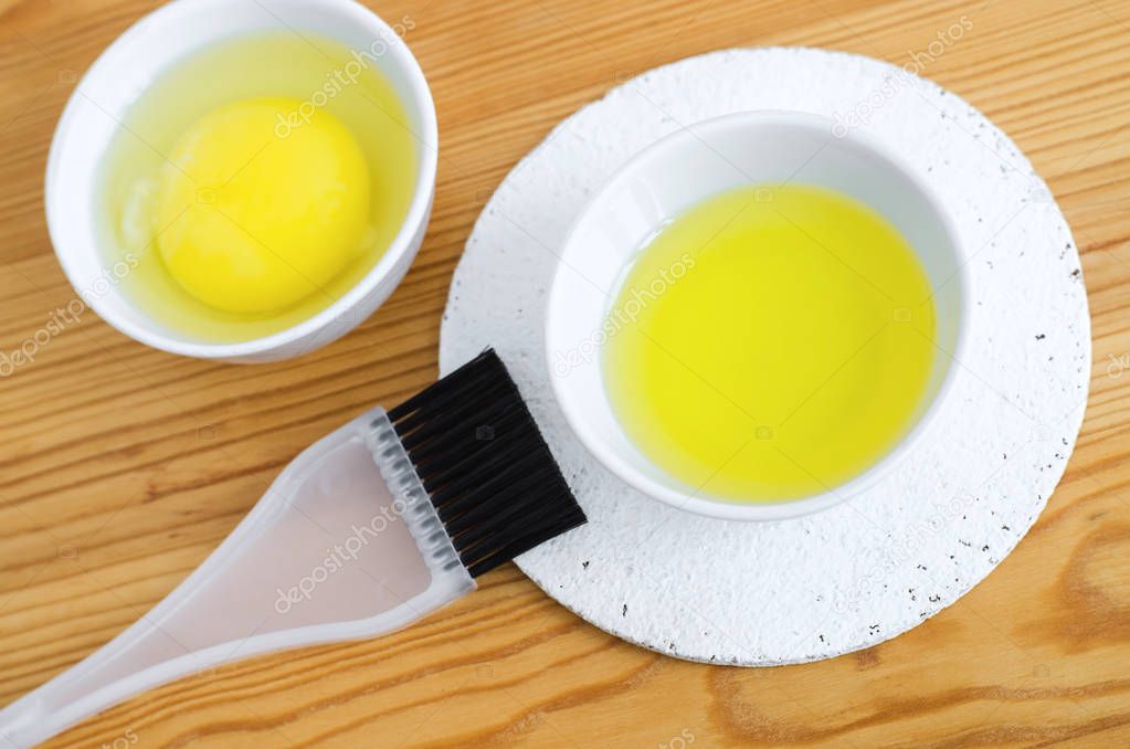 Olive oil and raw egg in a small ceramic bowls for preparing homemade spa face and hair masks. Ingredients for diy cosmetics.