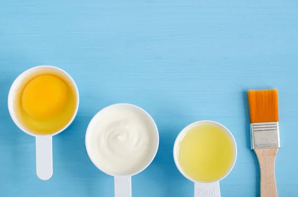 Krim asam (atau yogurt hijau), telur mentah dan minyak zaitun dalam satu sendok kecil. Bahan-bahan untuk menyiapkan masker, semak-semak, pelembab. Kosmetik buatan sendiri. Tampilan atas, ruang penyalinan . — Stok Foto