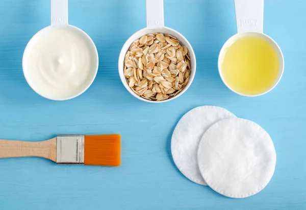 Krim asam (atau yogurt greek), oat gulung dan minyak zaitun dalam sendok plastik kecil - bahan-bahan untuk menyiapkan masker, semak belukar dan pelembab. Kosmetik buatan sendiri. Tampilan atas, ruang penyalinan . Stok Foto