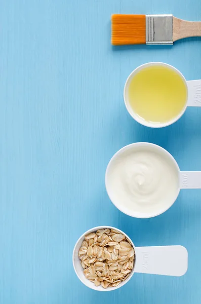 Krim asam (atau yogurt greek), oat gulung dan minyak zaitun dalam sendok plastik kecil - bahan-bahan untuk menyiapkan masker, semak belukar dan pelembab. Kosmetik buatan sendiri. Tampilan atas, ruang penyalinan . Stok Gambar Bebas Royalti