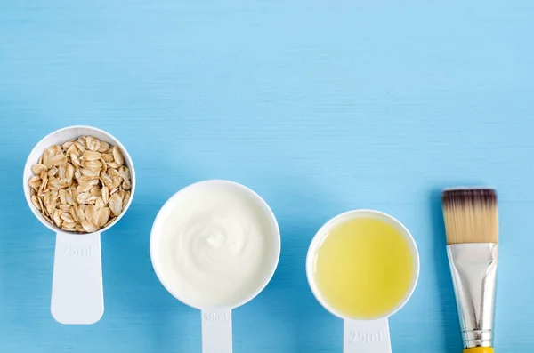 Krim asam (atau yogurt greek), oat gulung dan minyak zaitun dalam sendok plastik kecil - bahan-bahan untuk menyiapkan masker, semak belukar dan pelembab. Kosmetik buatan sendiri. Tampilan atas, ruang penyalinan . Stok Lukisan  