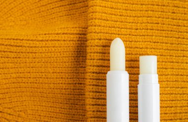 Two lip balms on the orange knitted background. Winter lip care sticks with beeswax, honey, panthenol and shea butter. Copy space.  clipart